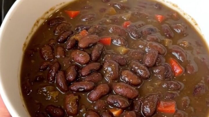 A top-down view of a black slow cooker filled with black bean stew and colorful red bell peppers.