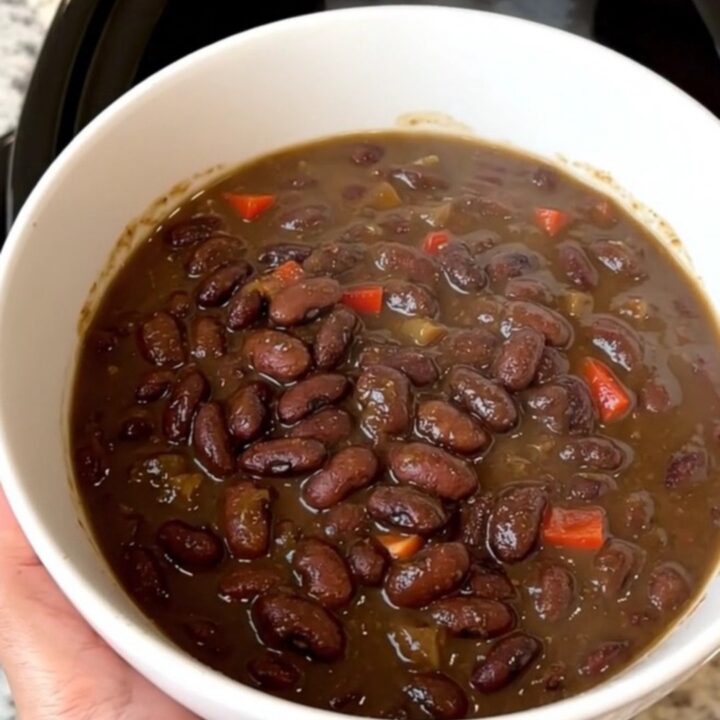 A top-down view of a black slow cooker filled with black bean stew and colorful red bell peppers.