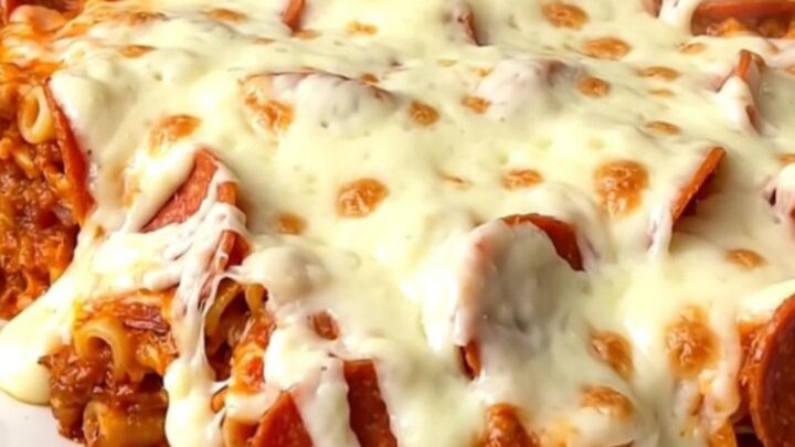 A top-down view of a slow cooker filled with ziti, pepperoni, and pizza sauce before cooking.