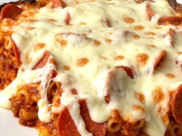 A top-down view of a slow cooker filled with ziti, pepperoni, and pizza sauce before cooking.