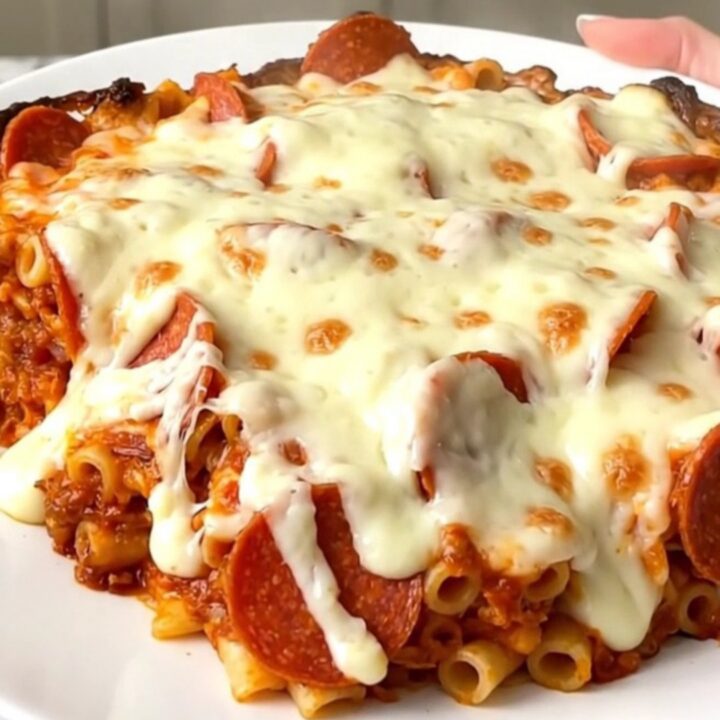 A top-down view of a slow cooker filled with ziti, pepperoni, and pizza sauce before cooking.
