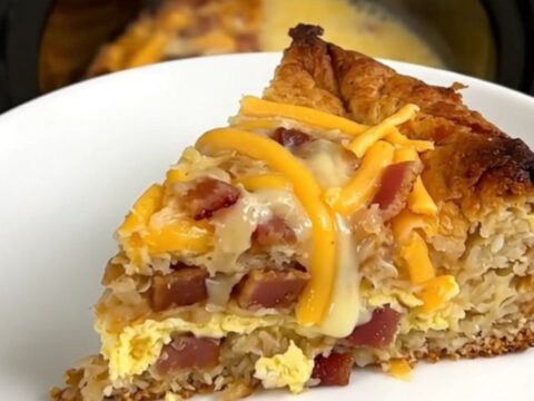 A warm, steaming slice of bacon and cheddar breakfast casserole on a white plate.