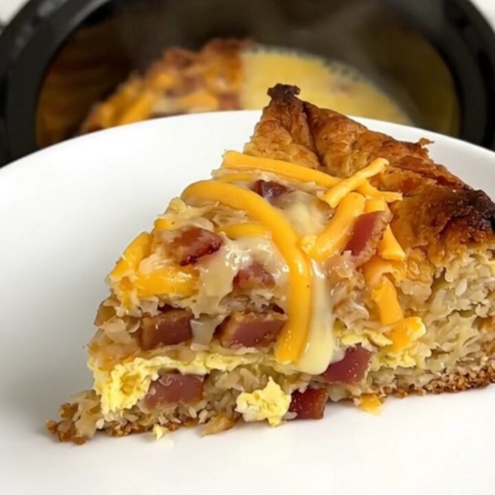 A warm, steaming slice of bacon and cheddar breakfast casserole on a white plate.