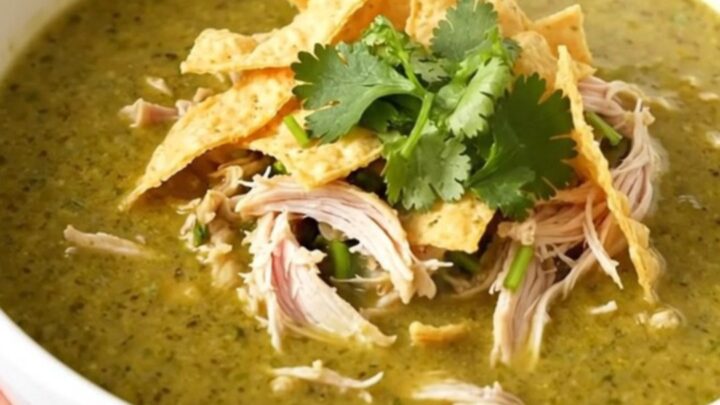 A steaming bowl of creamy green enchilada chicken soup topped with cilantro and tortilla strips.
