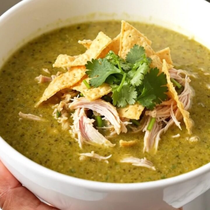 A steaming bowl of creamy green enchilada chicken soup topped with cilantro and tortilla strips.