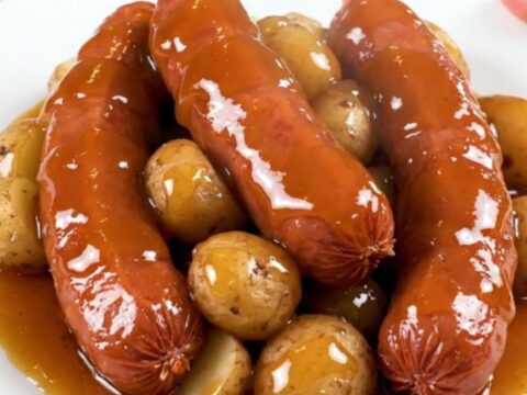 Slow cooker filled with sliced kielbasa and halved red potatoes coated in a glossy honey garlic sauce.