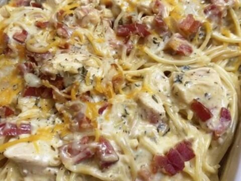 A golden-brown chicken spaghetti bake in a baking dish, topped with melted cheddar cheese and crispy bacon bits