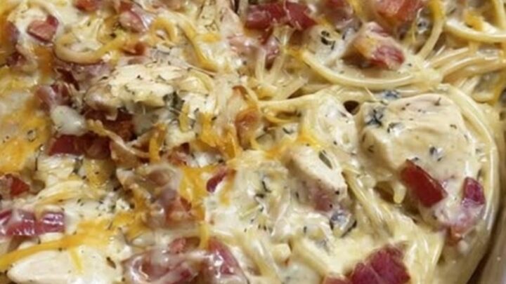 A golden-brown chicken spaghetti bake in a baking dish, topped with melted cheddar cheese and crispy bacon bits
