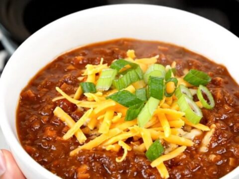 A bowl of rich honey chipotle beef chili topped with shredded cheese and fresh green scallions.