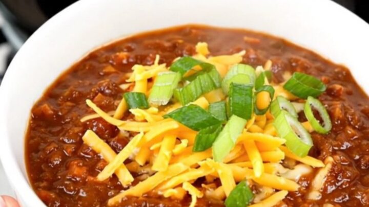 A bowl of rich honey chipotle beef chili topped with shredded cheese and fresh green scallions.