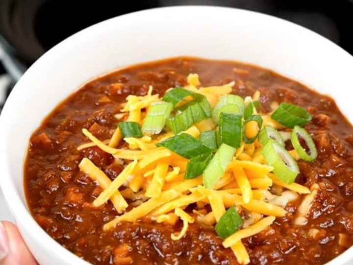 A bowl of rich honey chipotle beef chili topped with shredded cheese and fresh green scallions.
