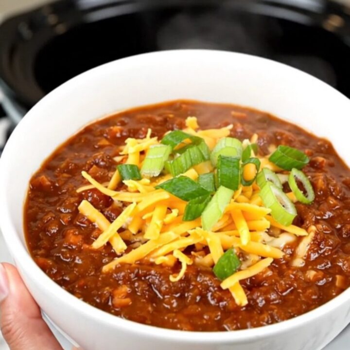 A bowl of rich honey chipotle beef chili topped with shredded cheese and fresh green scallions.