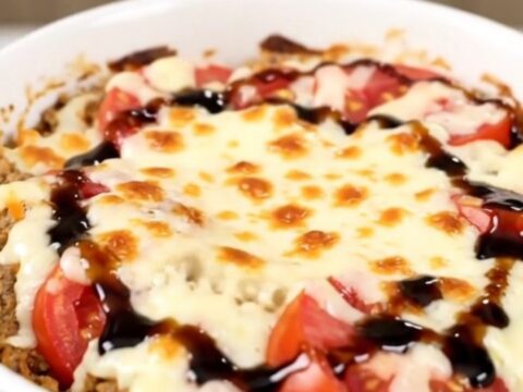 A top-down view of a black slow cooker filled with layers of tomatoes, fresh basil, and shredded mozzarella cheese.