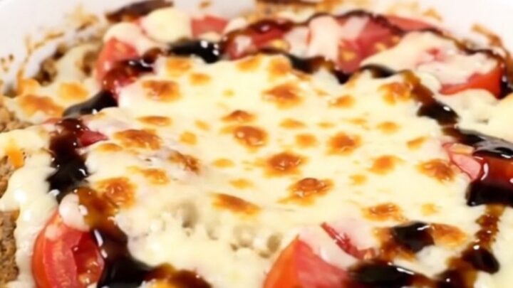 A top-down view of a black slow cooker filled with layers of tomatoes, fresh basil, and shredded mozzarella cheese.
