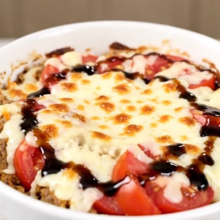 A top-down view of a black slow cooker filled with layers of tomatoes, fresh basil, and shredded mozzarella cheese.
