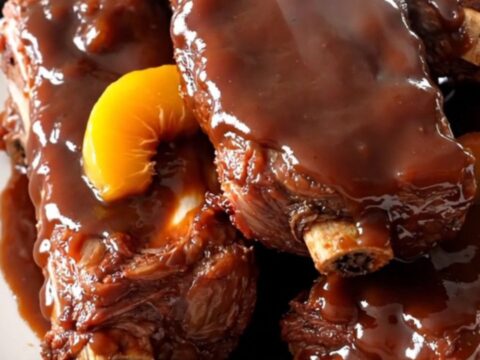 Slow cooked peach barbecue ribs served on a white plate with a glossy glaze.