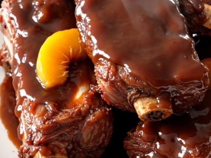 Slow cooked peach barbecue ribs served on a white plate with a glossy glaze.