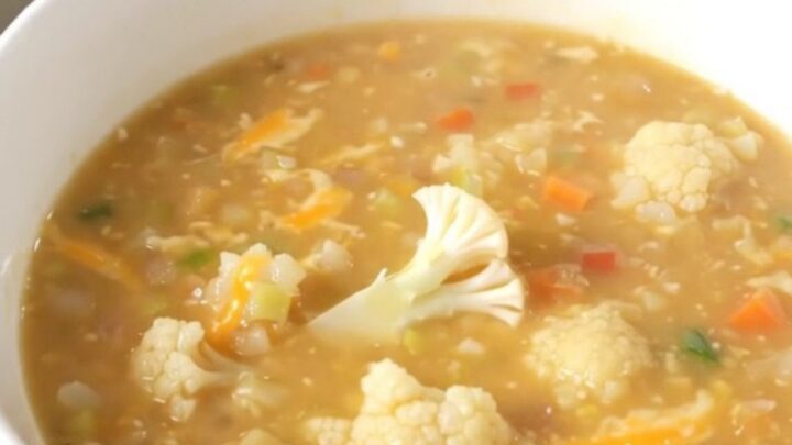 A steaming bowl of creamy cauliflower chowder garnished with fresh herbs on a wooden table.