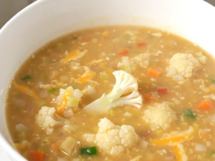 A steaming bowl of creamy cauliflower chowder garnished with fresh herbs on a wooden table.