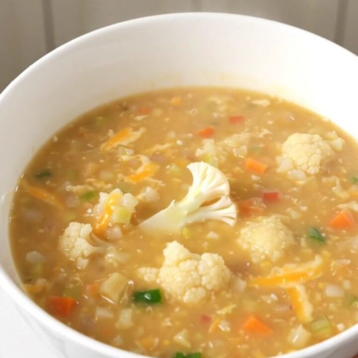 A steaming bowl of creamy cauliflower chowder garnished with fresh herbs on a wooden table.