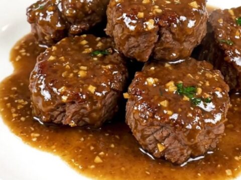 A close-up of glossy garlic parmesan steak bites served on a white plate.