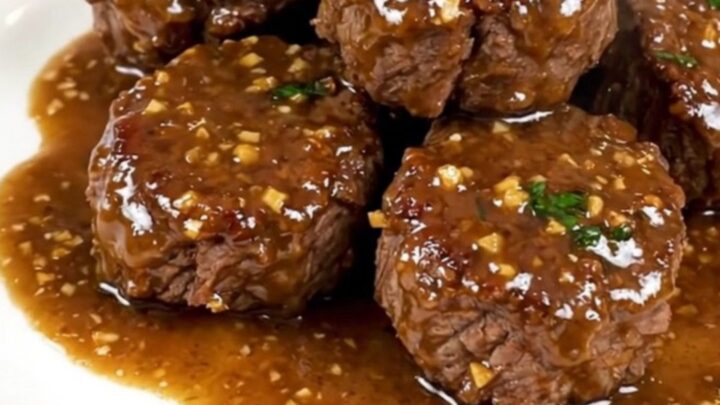 A close-up of glossy garlic parmesan steak bites served on a white plate.