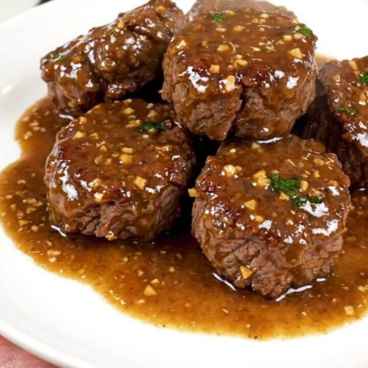 A close-up of glossy garlic parmesan steak bites served on a white plate.