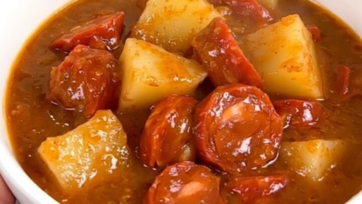A steaming, glossy bowl of Mexican chorizo and potato stew held by a hand in a bright kitchen.