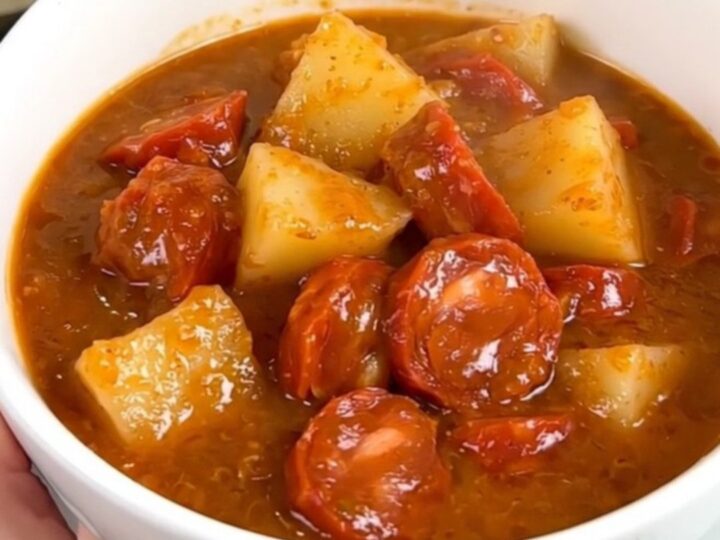 A steaming, glossy bowl of Mexican chorizo and potato stew held by a hand in a bright kitchen.