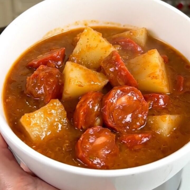 A steaming, glossy bowl of Mexican chorizo and potato stew held by a hand in a bright kitchen.