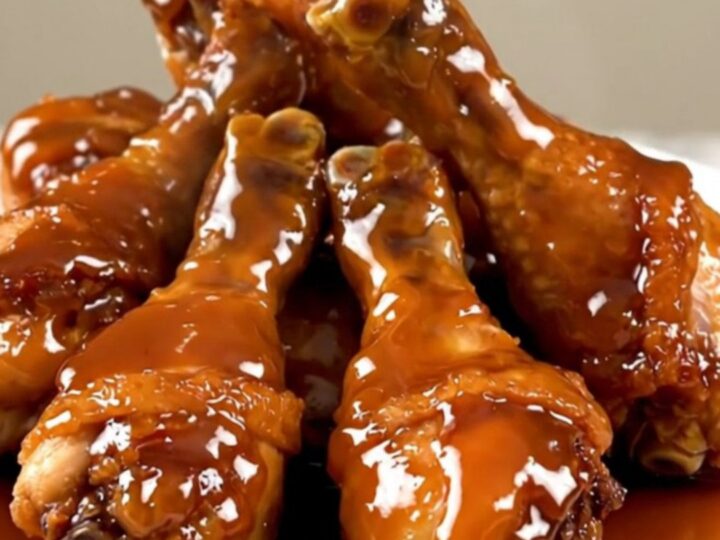 Close up overhead shot of slow cooker filled with raw chicken drumsticks and sliced shallots.