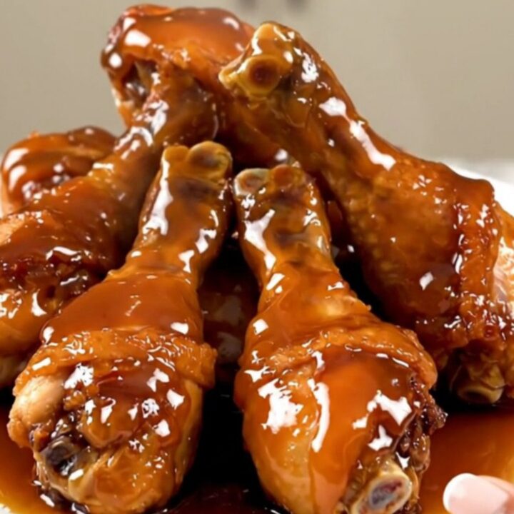 Close up overhead shot of slow cooker filled with raw chicken drumsticks and sliced shallots.