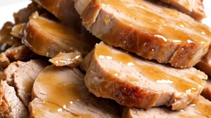 A close-up of sliced pork tenderloin medallions glazed in a glossy apricot ginger sauce on a white plate.