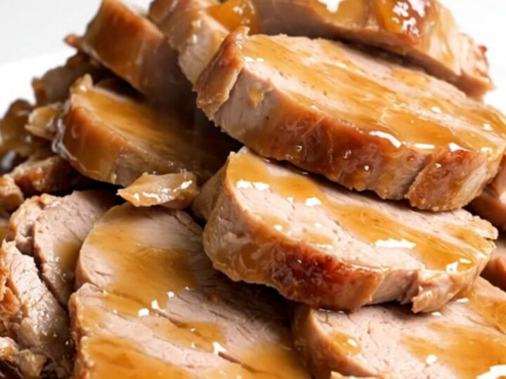 A close-up of sliced pork tenderloin medallions glazed in a glossy apricot ginger sauce on a white plate.