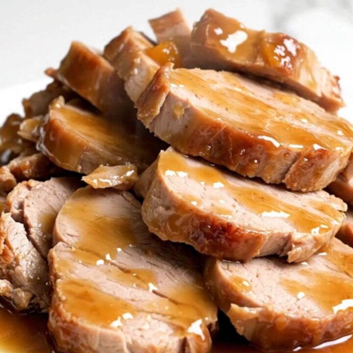 A close-up of sliced pork tenderloin medallions glazed in a glossy apricot ginger sauce on a white plate.