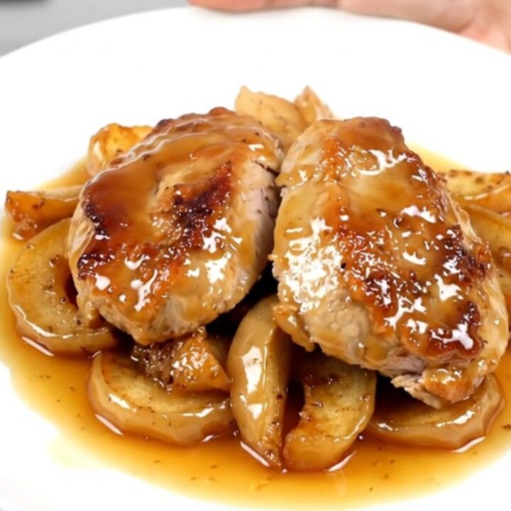 A close-up of sliced turkey medallions topped with spiced apples on a white plate.