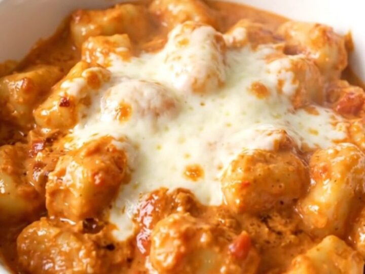 A white bowl filled with creamy tomato basil gnocchi topped with melted mozzarella cheese.
