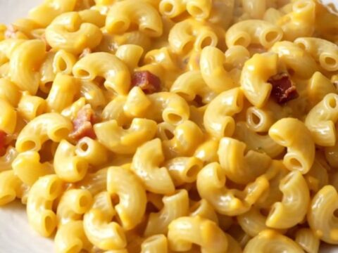 A slow cooker filled with creamy macaroni and cheese featuring visible bacon bits and a hint of smoked paprika.