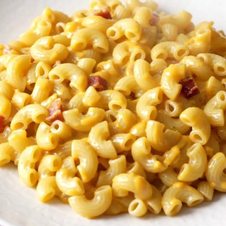 A slow cooker filled with creamy macaroni and cheese featuring visible bacon bits and a hint of smoked paprika.