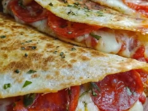 A stack of golden, crispy pepperoni pizza quesadillas on a wooden board, showing a cheese pull.