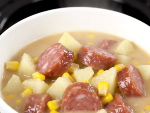 A rustic black slow cooker filled with a creamy smoked sausage and potato chowder, ready to be served.
