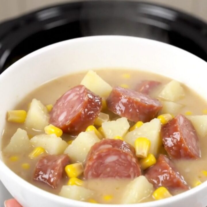 A rustic black slow cooker filled with a creamy smoked sausage and potato chowder, ready to be served.