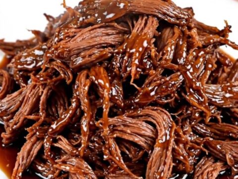 A close-up of tender, shredded beef coated in a dark, glossy honey soy glaze on a white plate.