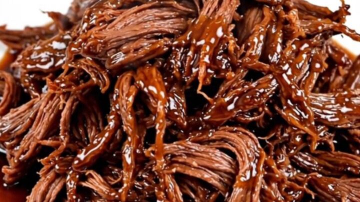A close-up of tender, shredded beef coated in a dark, glossy honey soy glaze on a white plate.
