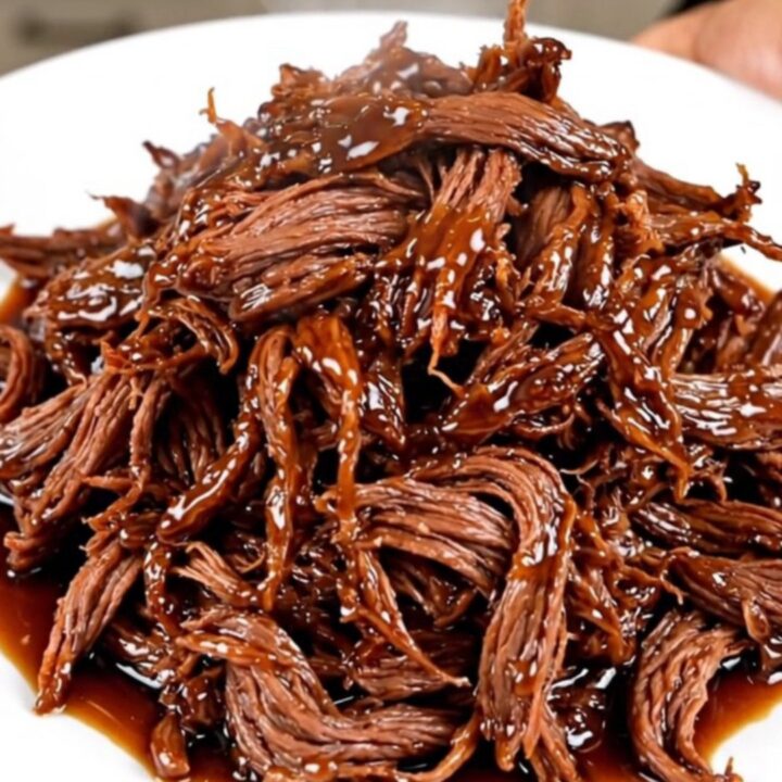 A close-up of tender, shredded beef coated in a dark, glossy honey soy glaze on a white plate.