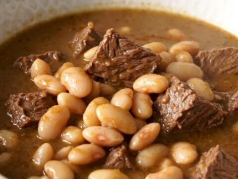 A steaming bowl of Italian beef and white bean stew on a table.