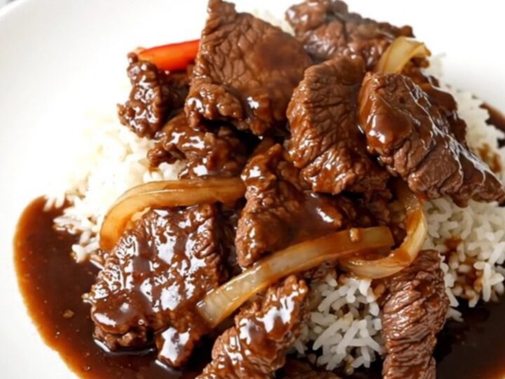 A top-down view of a slow cooker filled with tender beef strips, sliced bell peppers, and onions in a rich, glossy sauce.