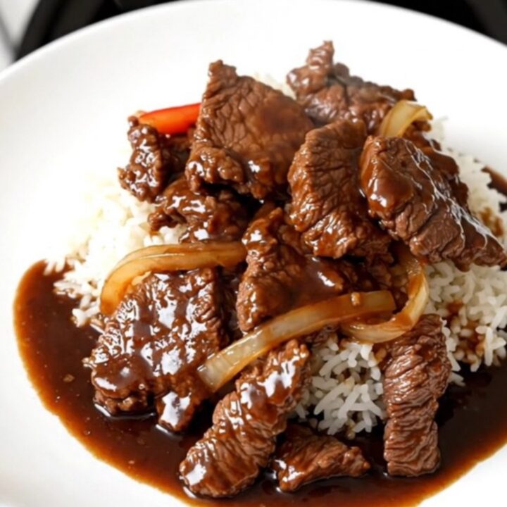 A top-down view of a slow cooker filled with tender beef strips, sliced bell peppers, and onions in a rich, glossy sauce.