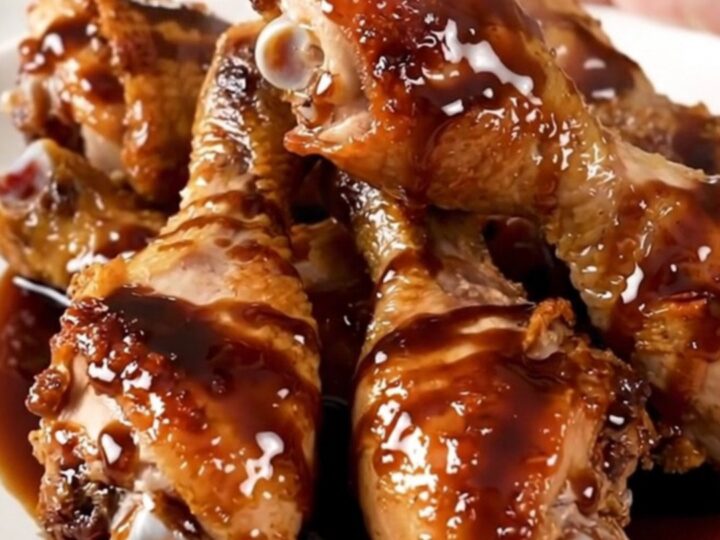 A plate of glossy, dark balsamic glazed chicken drumsticks with tender baby carrots.