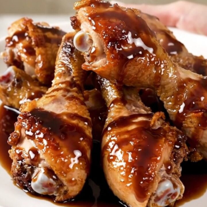 A plate of glossy, dark balsamic glazed chicken drumsticks with tender baby carrots.